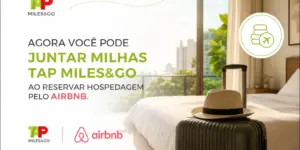 Quarto de hotel com mala e chapéu, vista de cidade à noite. Milhas e hospedagem.
